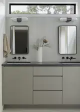 Primary bathroom featuring a double vanity set against a textured large-format wall tiles. The existing window was raised to clerestory height to allow for mirrors and lighting above the sinks, bringing soft natural light across the space while preserving privacy.
