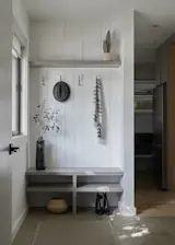 The wall dividing the old laundry room and breakfast nook was removed to form a connected mudroom and pantry area. A built-in bench, hooks, and soft vertical paneling bring structure and warmth to the new drop zone.