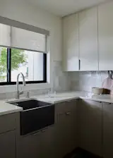 “Former laundry room reworked into a bright prep area, with a farmhouse-style sink positioned under the existing window and new cabinetry designed around that constraint. Moroccan tile adds a subtle handmade texture that softens the modern, matte finishes.