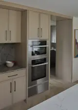 Built-in Miele appliances sit within custom red oak cabinetry, with the passage to the pantry and mudroom similarly wrapped to create continuity. The warm wood tone visually links the kitchen with the secondary work-spaces beyond.